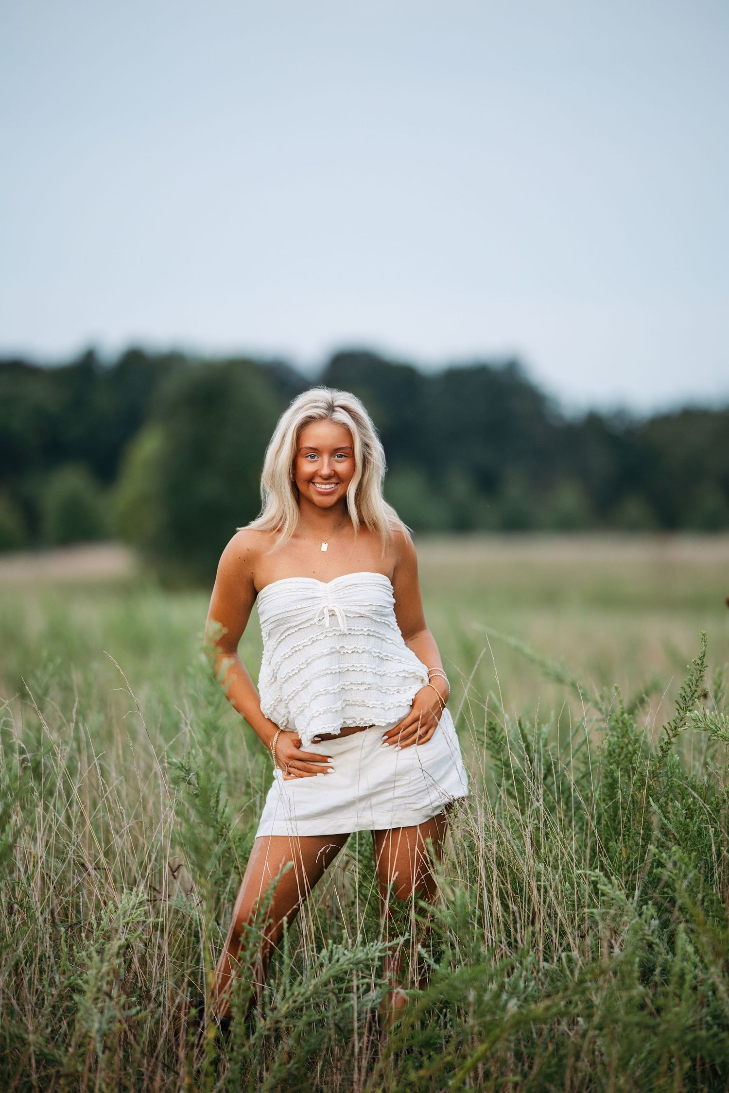 A person wrapped in white fabric poses playfully in a tall grass field on a summer day.