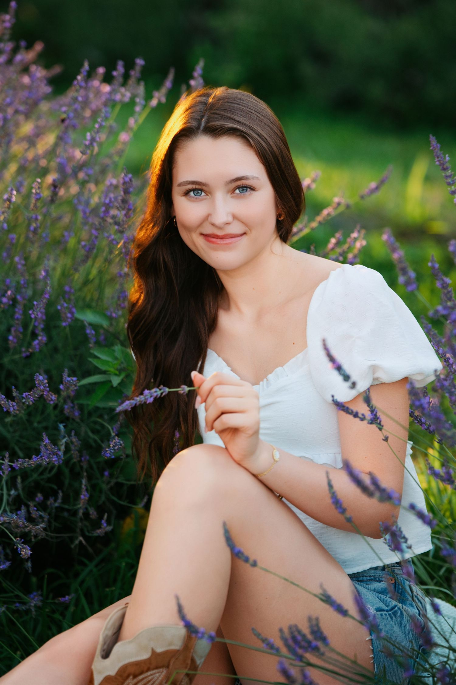 A woman in a white dress poses gracefully among blooming purple lavender flowers in a garden setting.