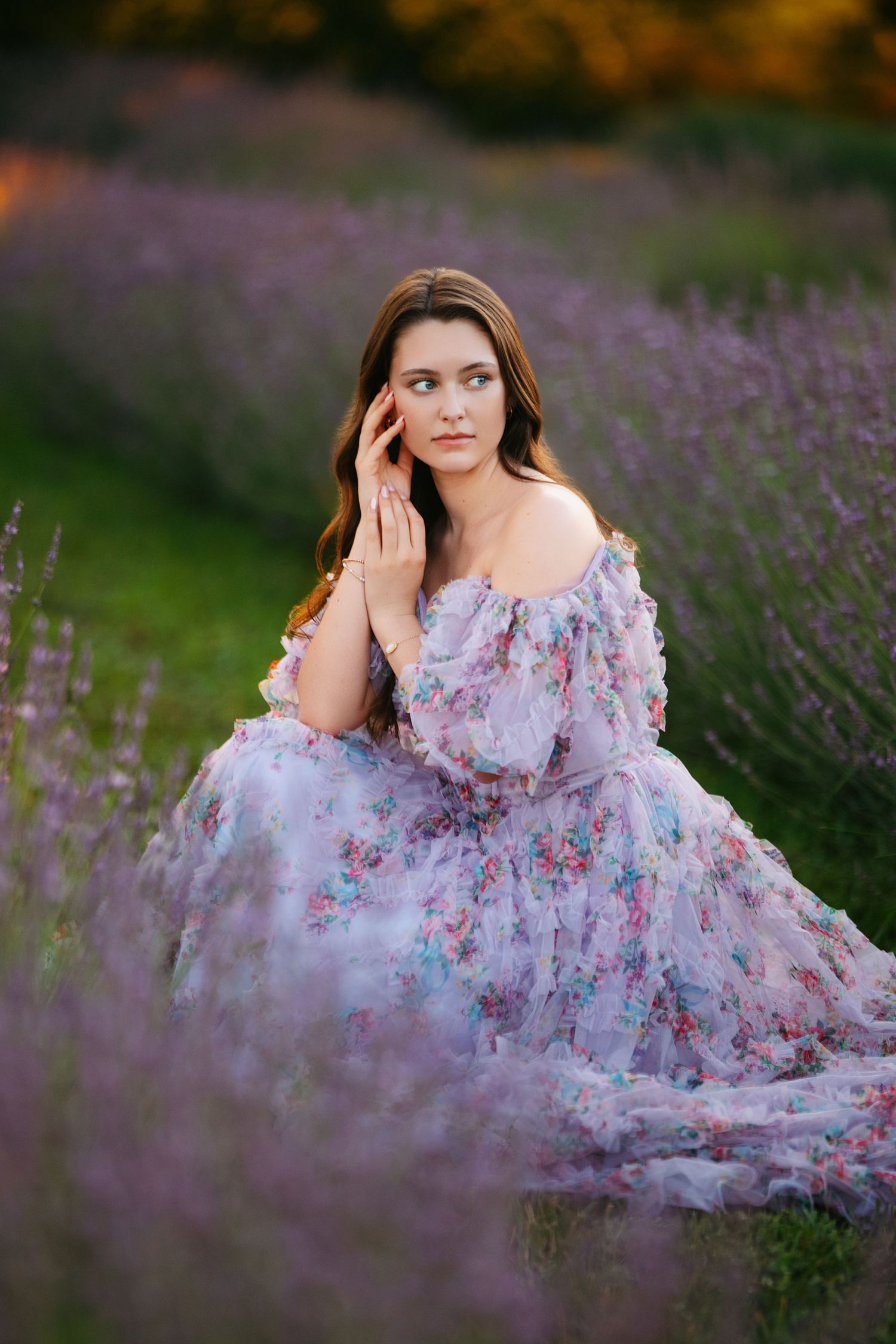 A person in a floral dress poses gracefully among blooming lavender fields at sunset.