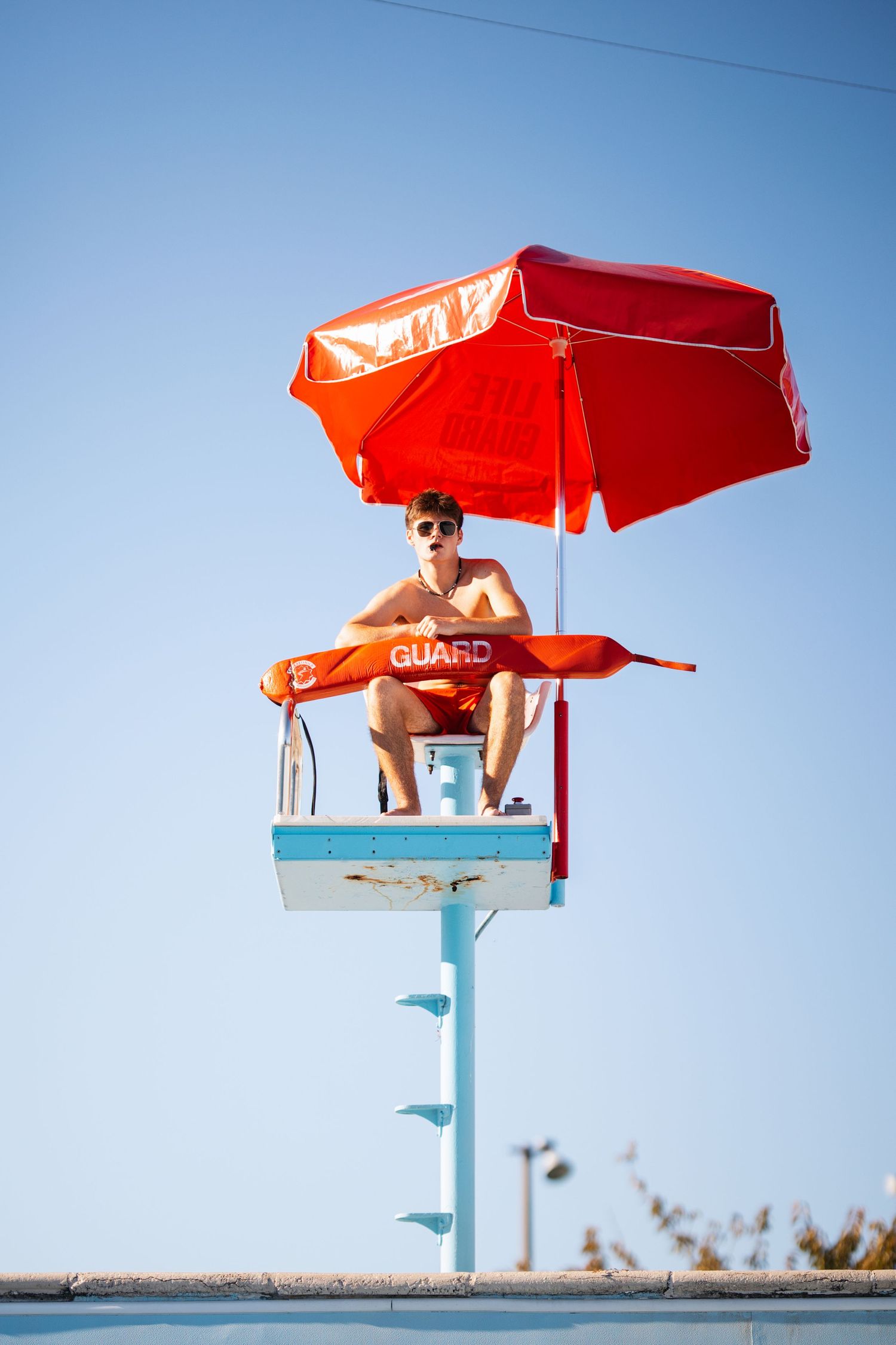 Lifeguard station with red umbrella and senior guy against bright blue sky in Nashville.  Middle TN senior photographer.