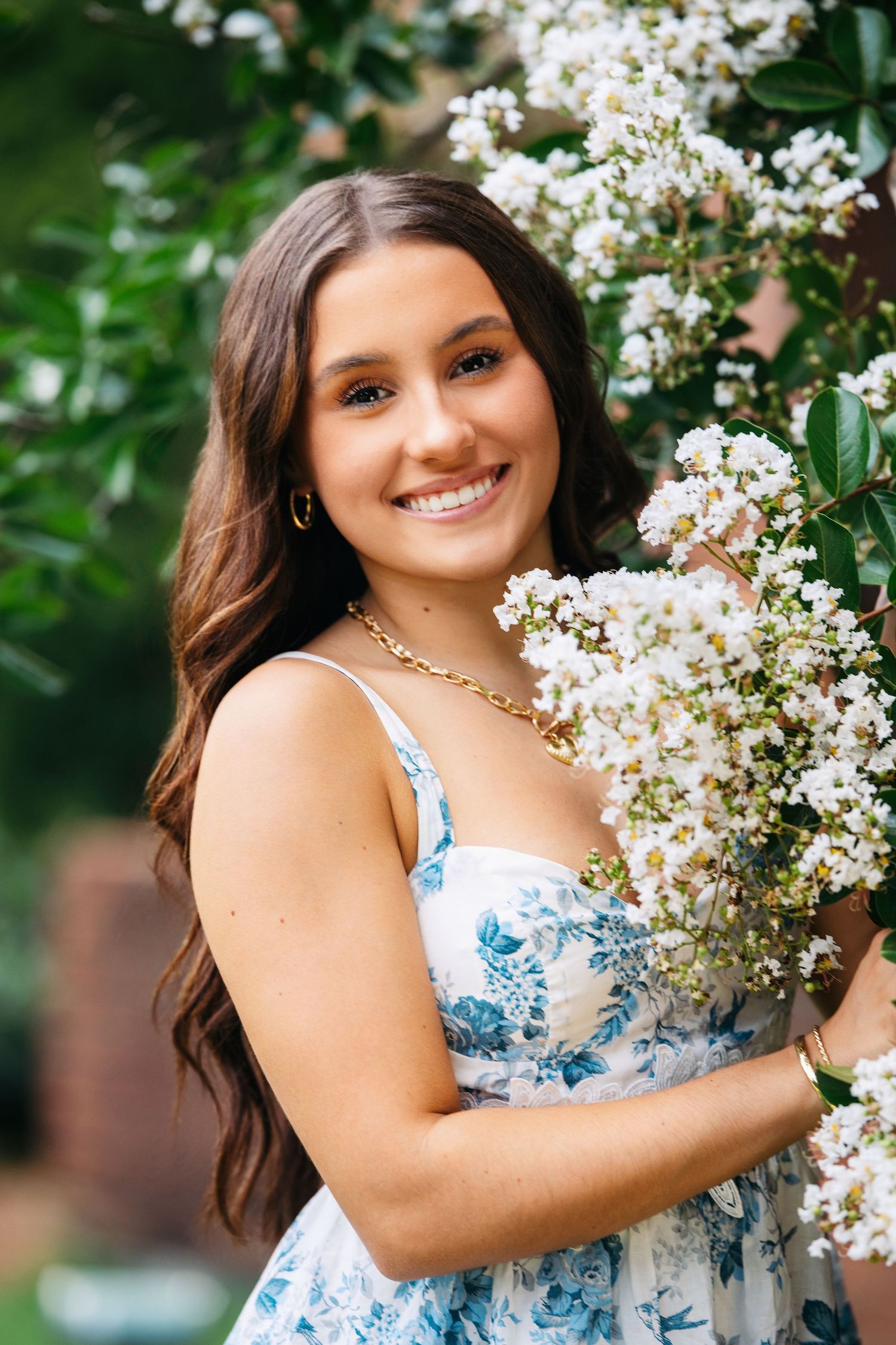 A floral portrait session in a garden setting with white crepe myrtle blooms and a blue and white floral dress.
