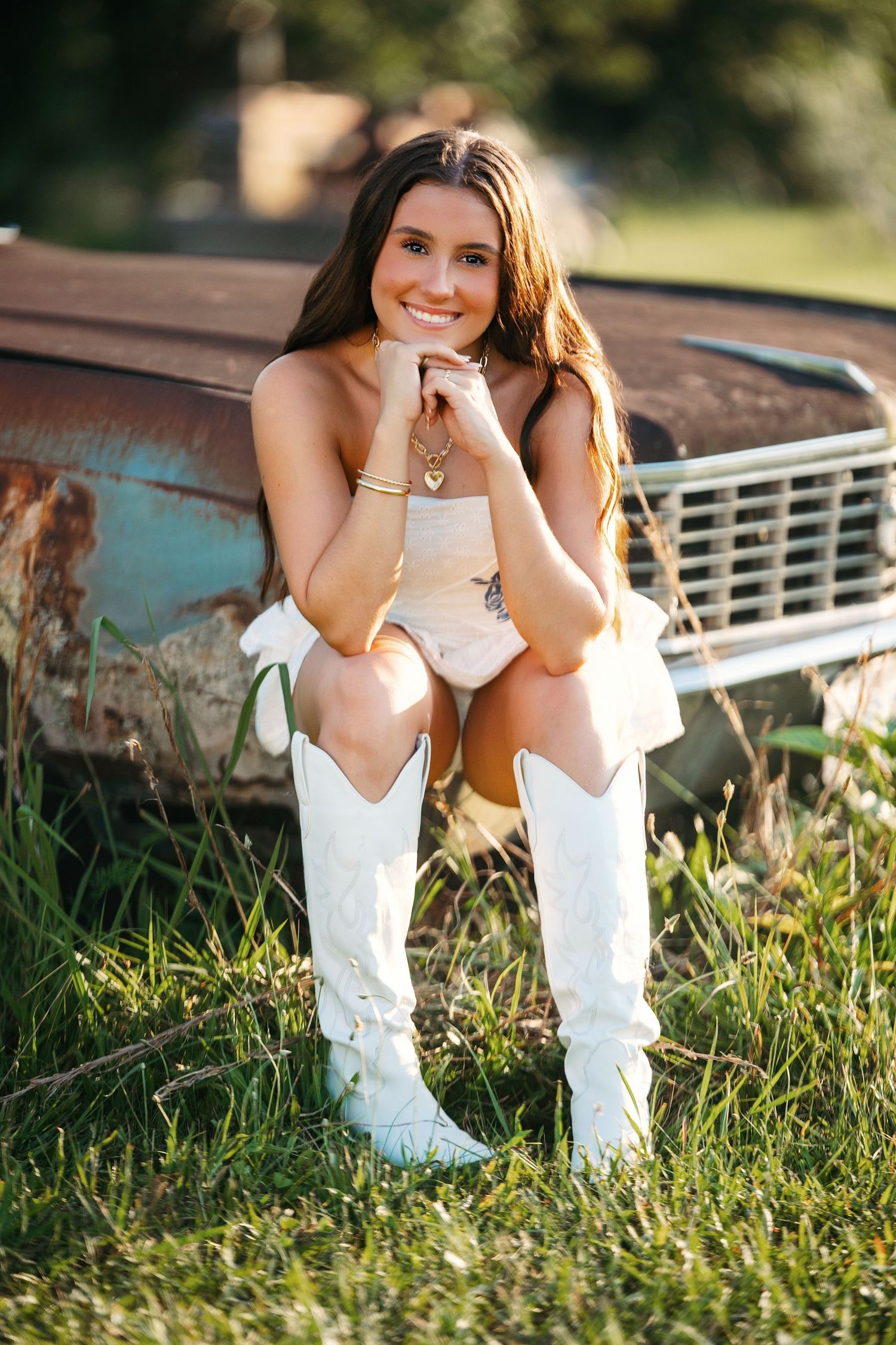 White cowboy boots in tall grass with rustic wooden fence in background during golden hour sunset.
