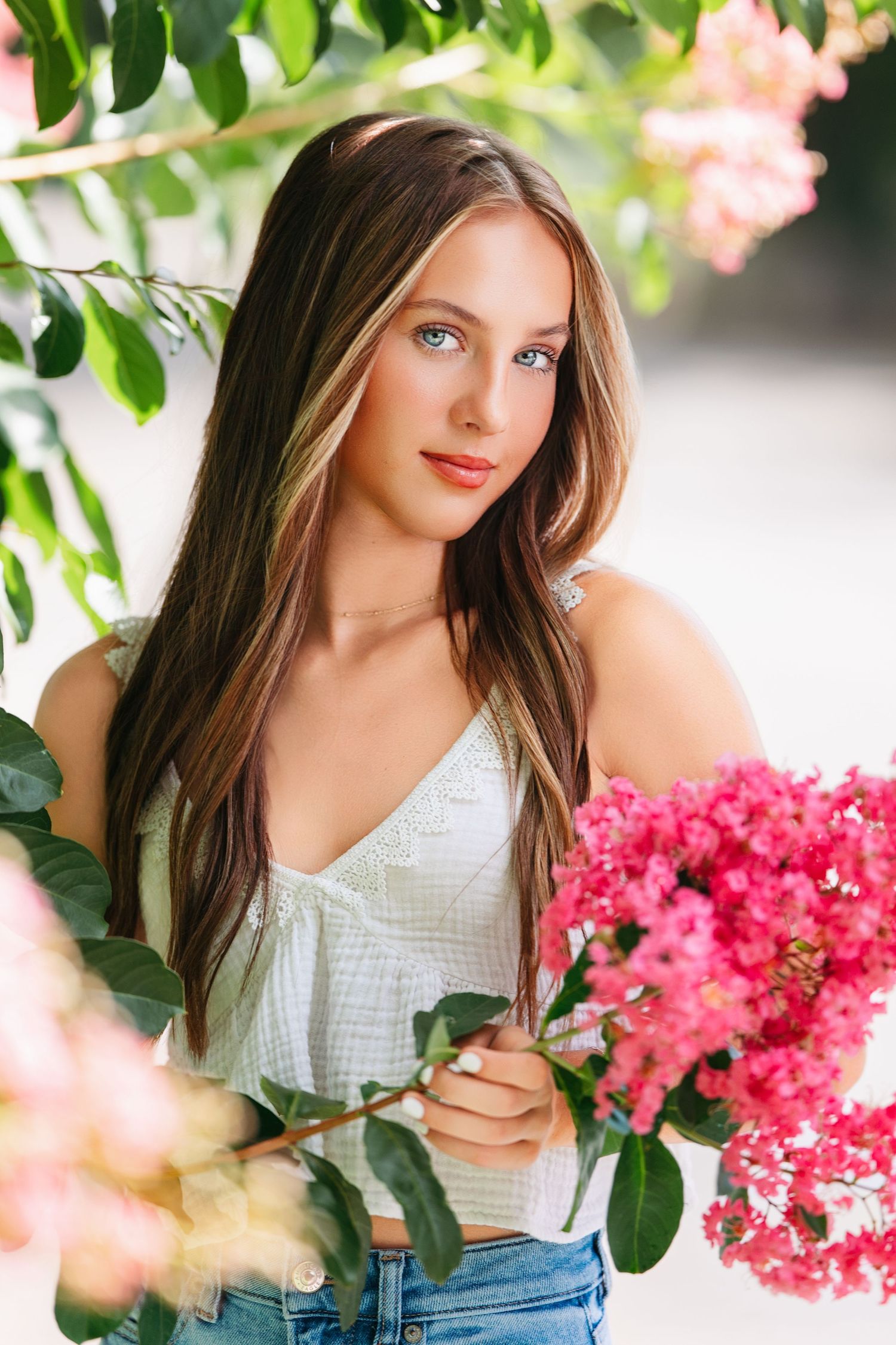 A portrait of a person in a white top posing with pink flowers in a garden setting.