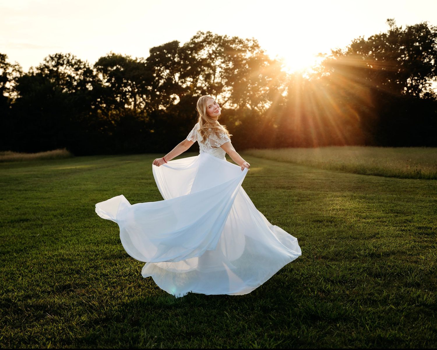 Flowing white dress twirls gracefully in golden sunset light across grassy field. Middle TN Senior photographer