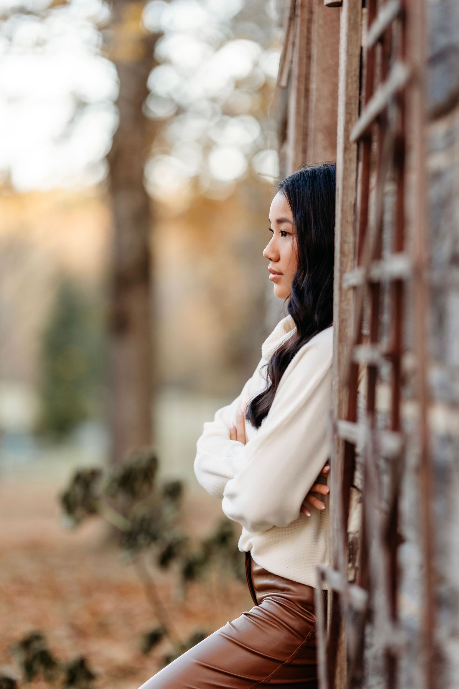 senior in white sweater and brown pants posing against wooden fence during autumn. Middle TN Senior photographer