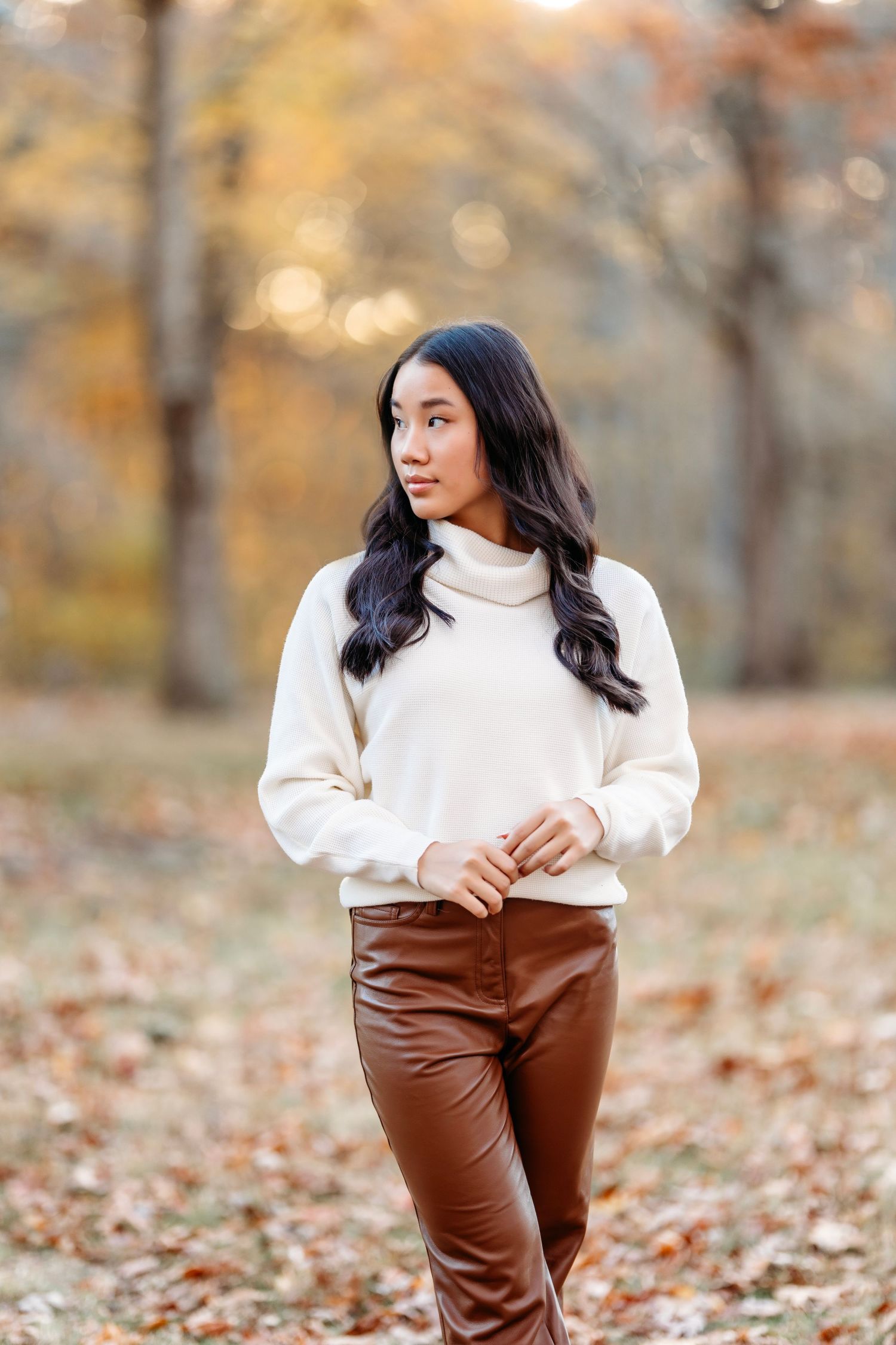 senior in cream turtleneck and brown pants walking through fallen autumn leaves.Middle TN Senior photographer