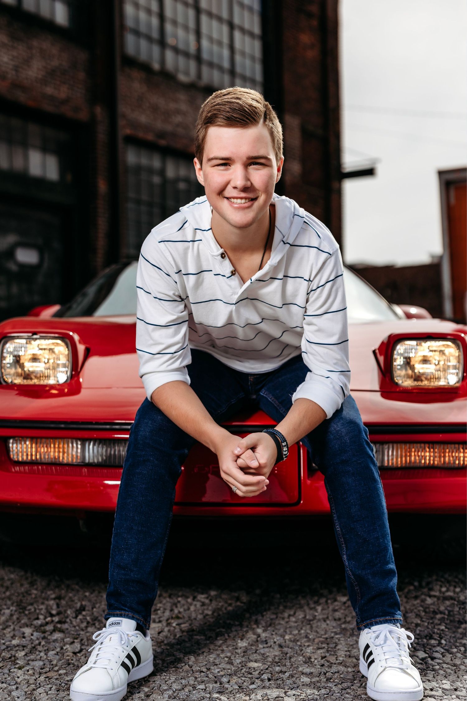 Young man in striped shirt sitting on hood of red sports car. Middle TN Senior photographer