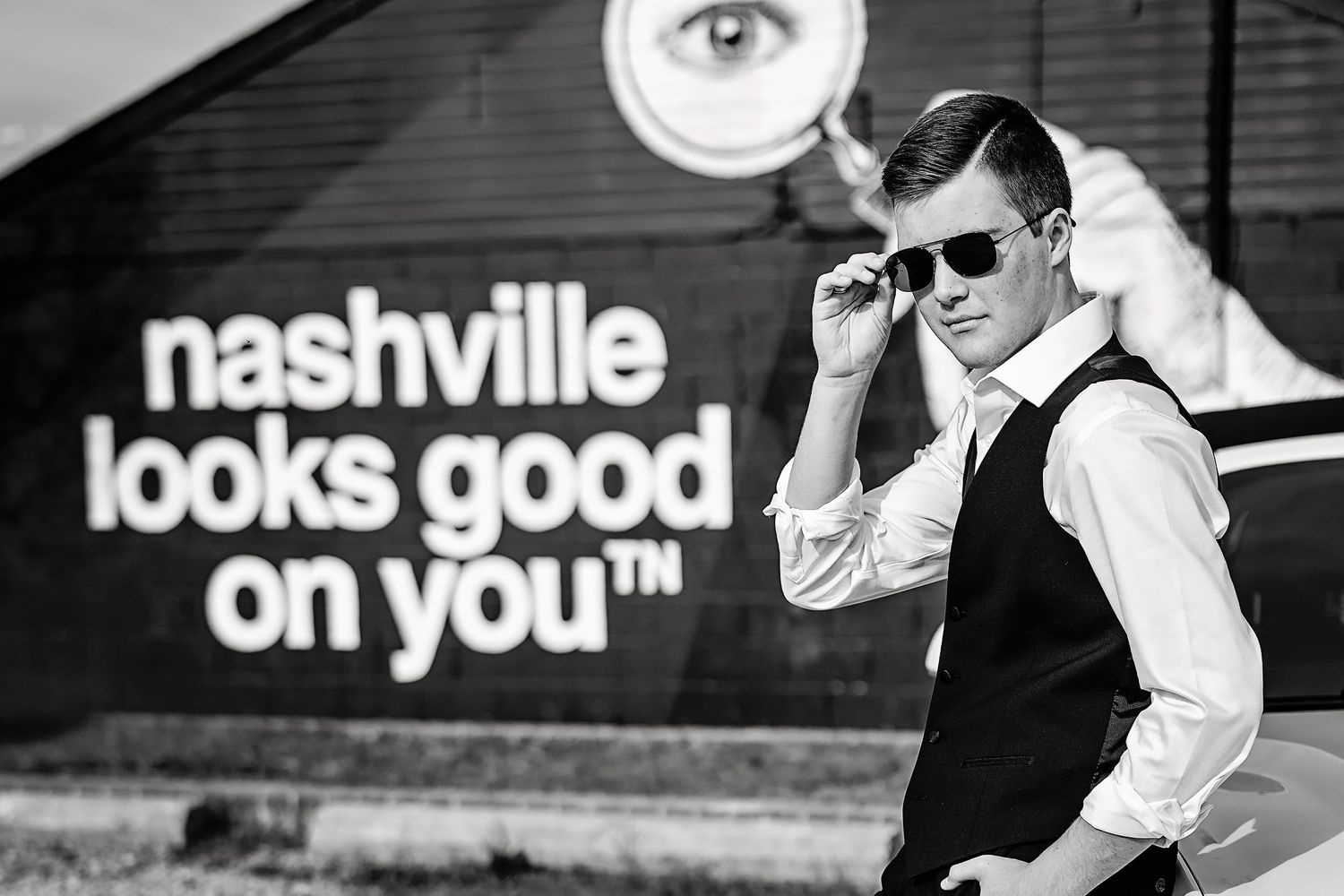 Stylish man in vest adjusting sunglasses in front of Nashville mural. Middle TN Senior photographer