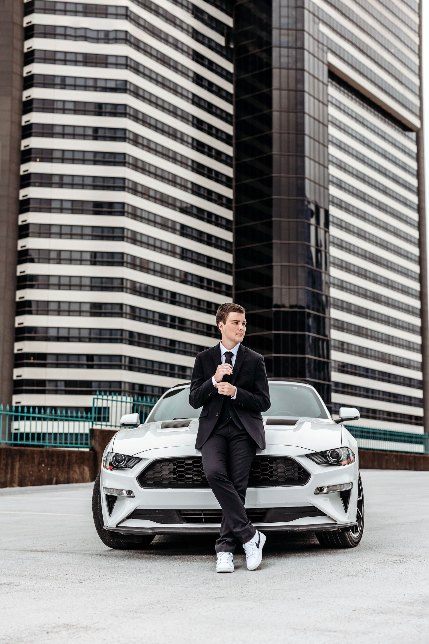 Stylish man in black suit poses with luxury white car against modern architectural backdrop.Middle TN Senior photographer