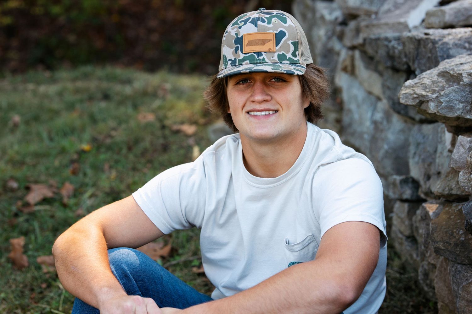 Relaxed outdoor portrait against a stone wall wearing a decorative hat. Middle TN senior photographer.