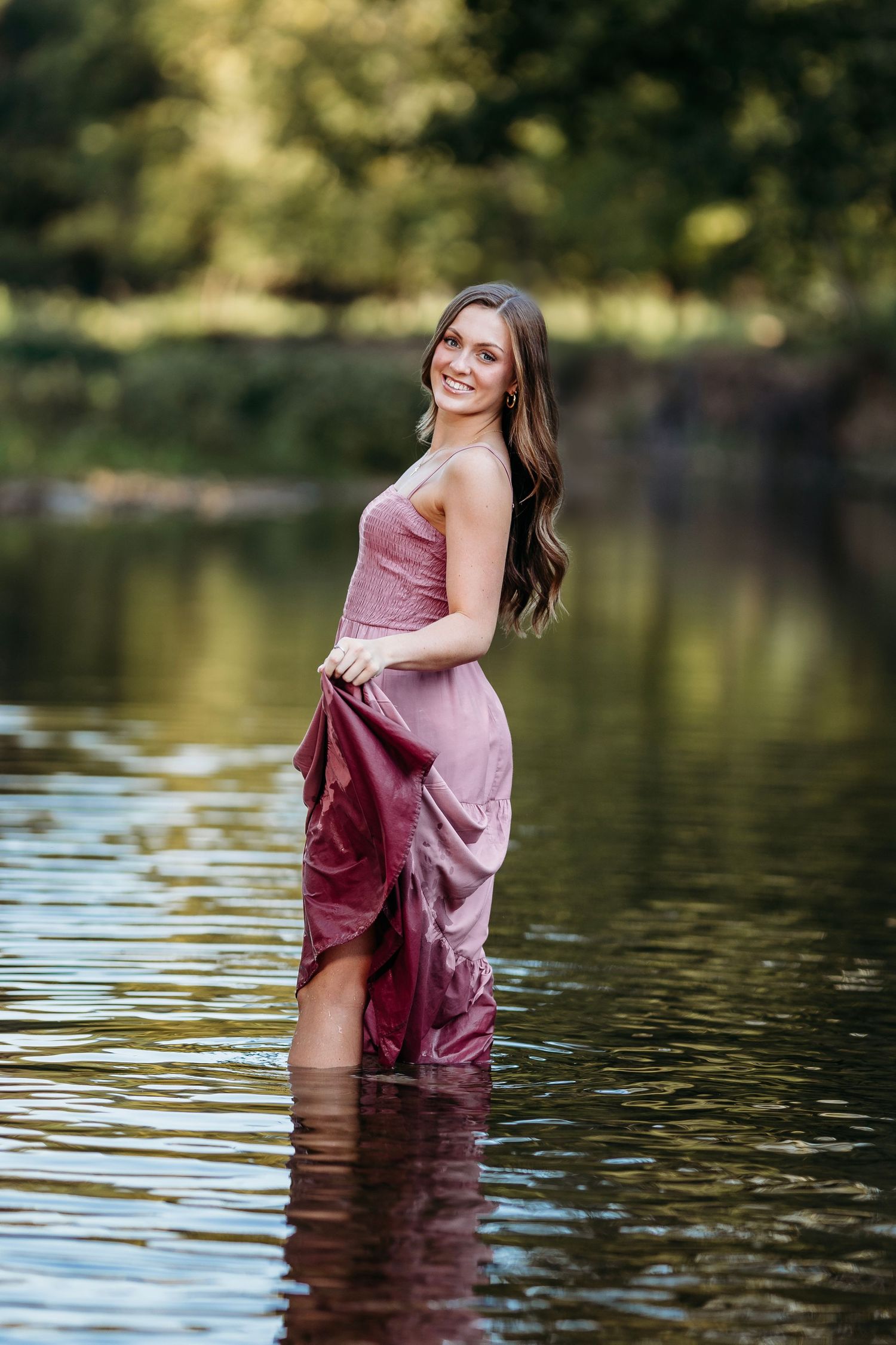 Senior girl in a burgundy dress standing in a serene lake during golden hour with reflective water.Middle TN Senior photographer