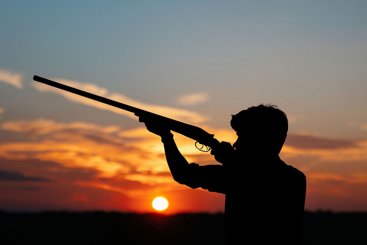 Silhouette of hunter with rifle against dramatic sunset sky with senior guy.  Middle TN senior photographer.