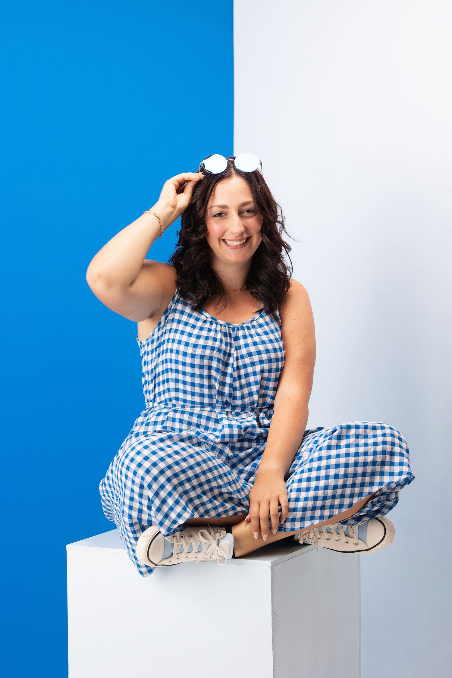 Cheerful pose in blue gingham jumpsuit against blue and white background. Middle TN senior photographer.