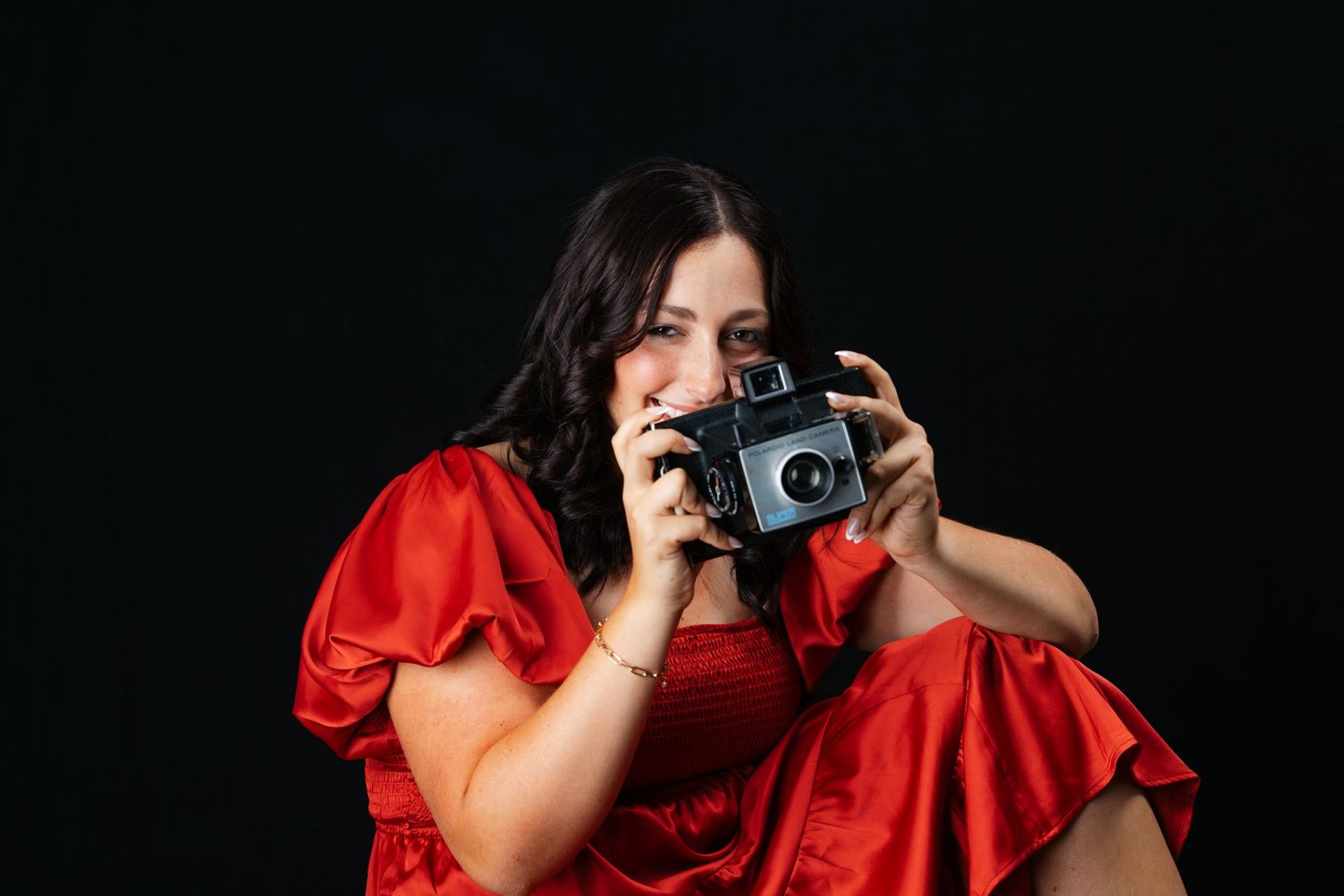 Portrait with vintage camera wearing dramatic red dress against black background. Middle TN senior photographer.