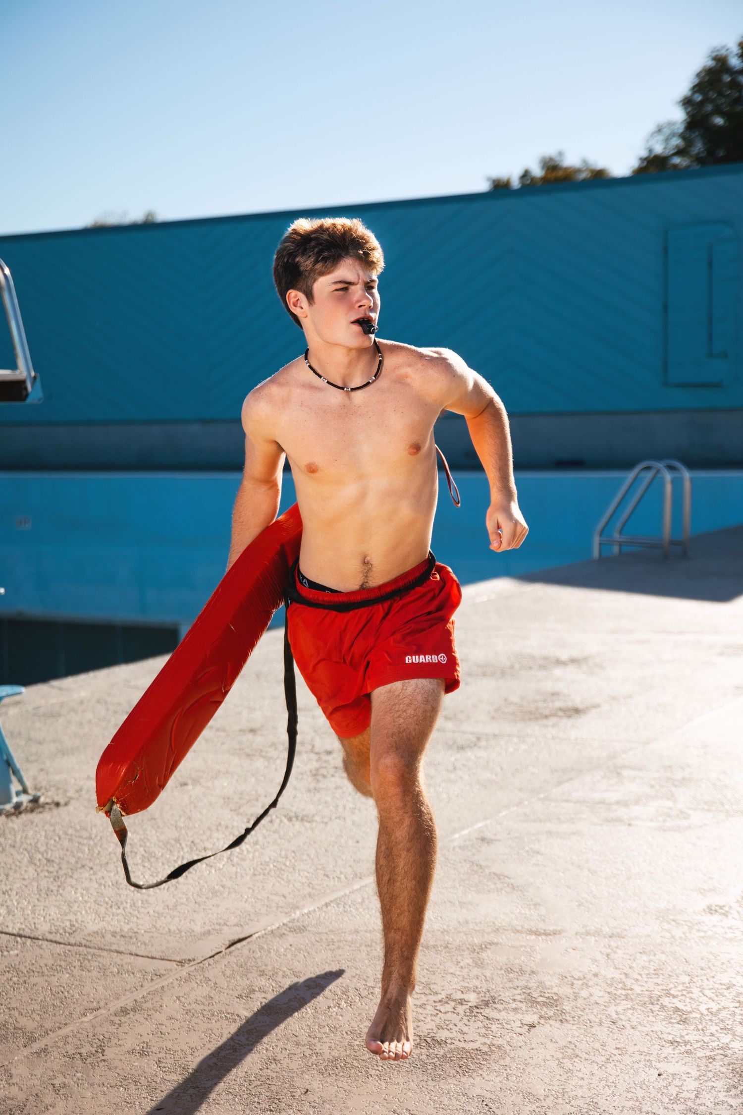 Senior guy lifeguard in red shorts running across a bright sunny concrete surface. Middle TN senior photographer.