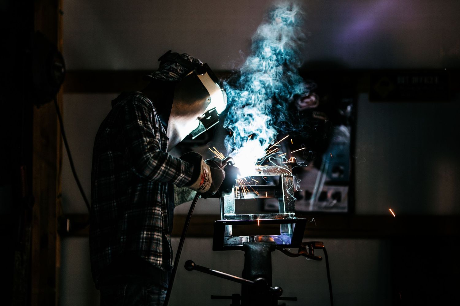 Sparks fly as a welder works in a dark workshop with blue light illuminating the metalworking process.
