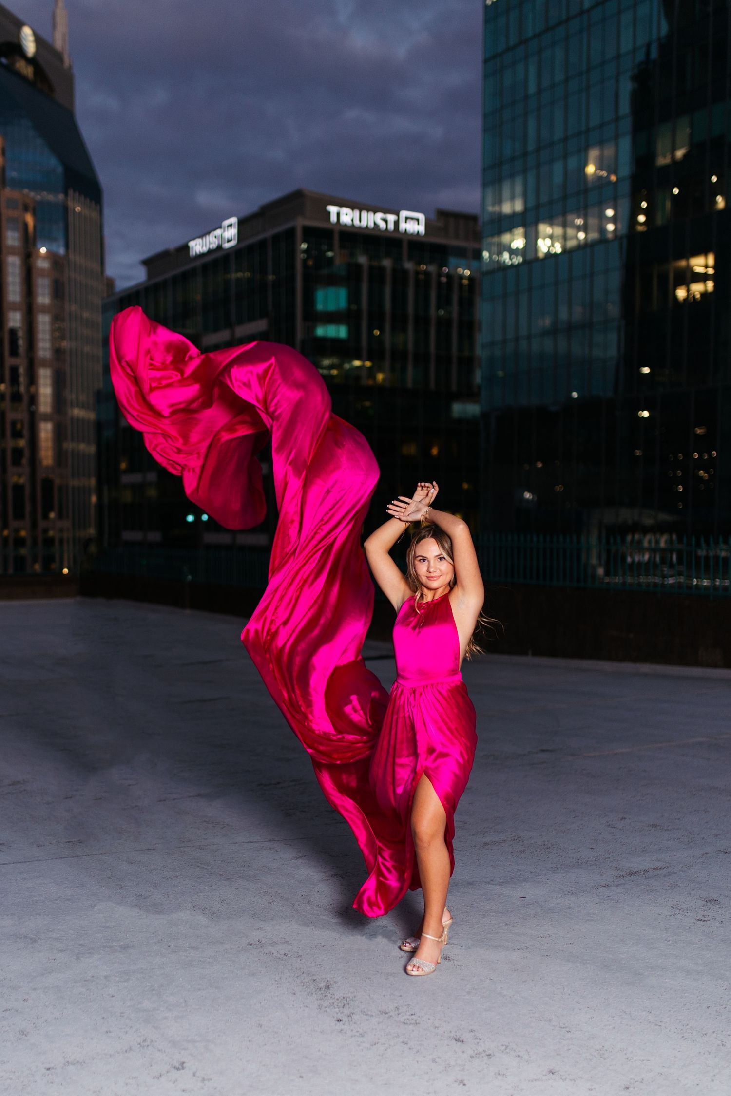 Dynamic fashion shoot with flowing hot pink dress against urban nighttime backdrop. Middle TN senior photographer.