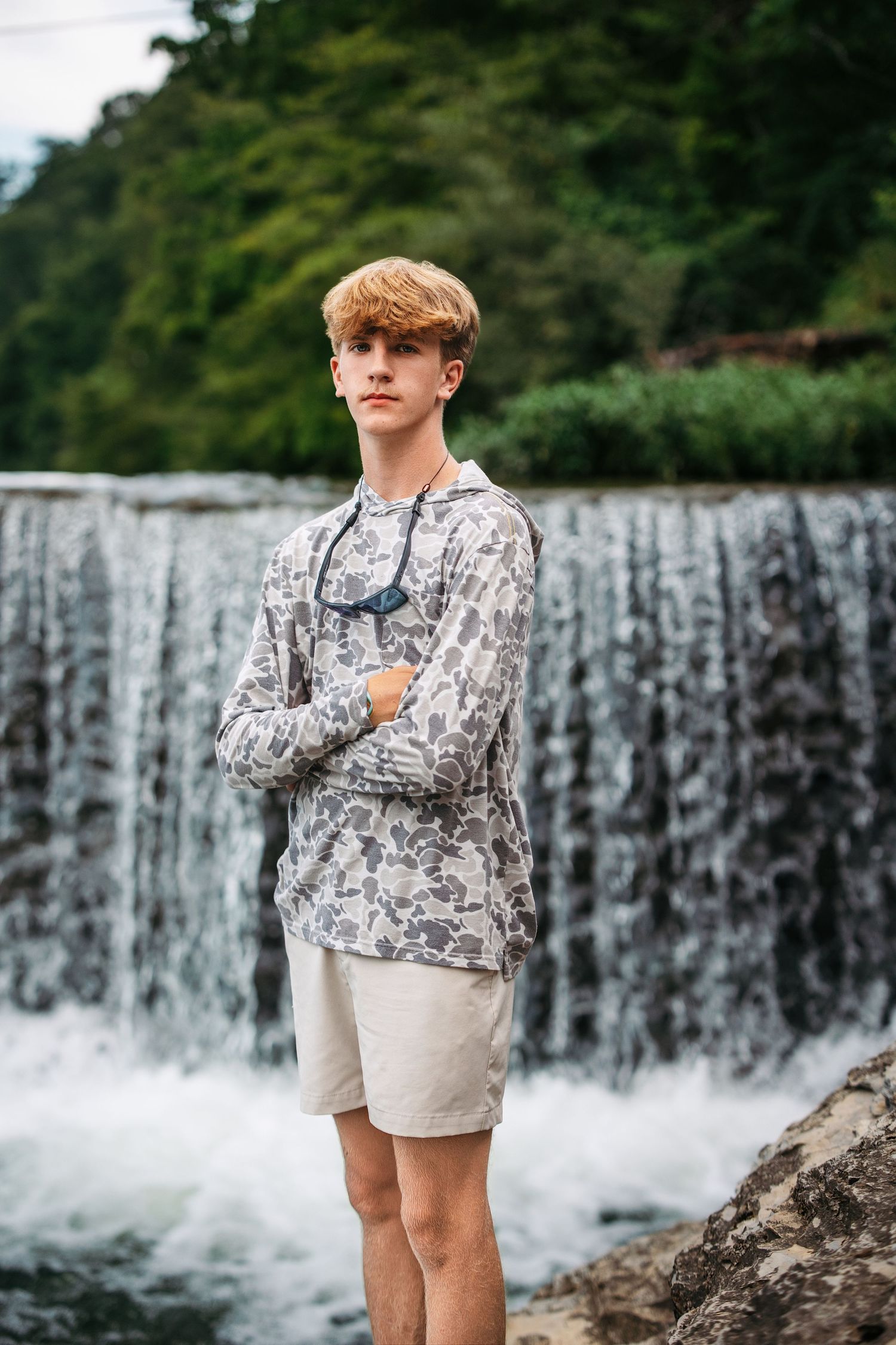 A series of photos showing someone in a gray sweater posing near a cascading waterfall on a cloudy day.