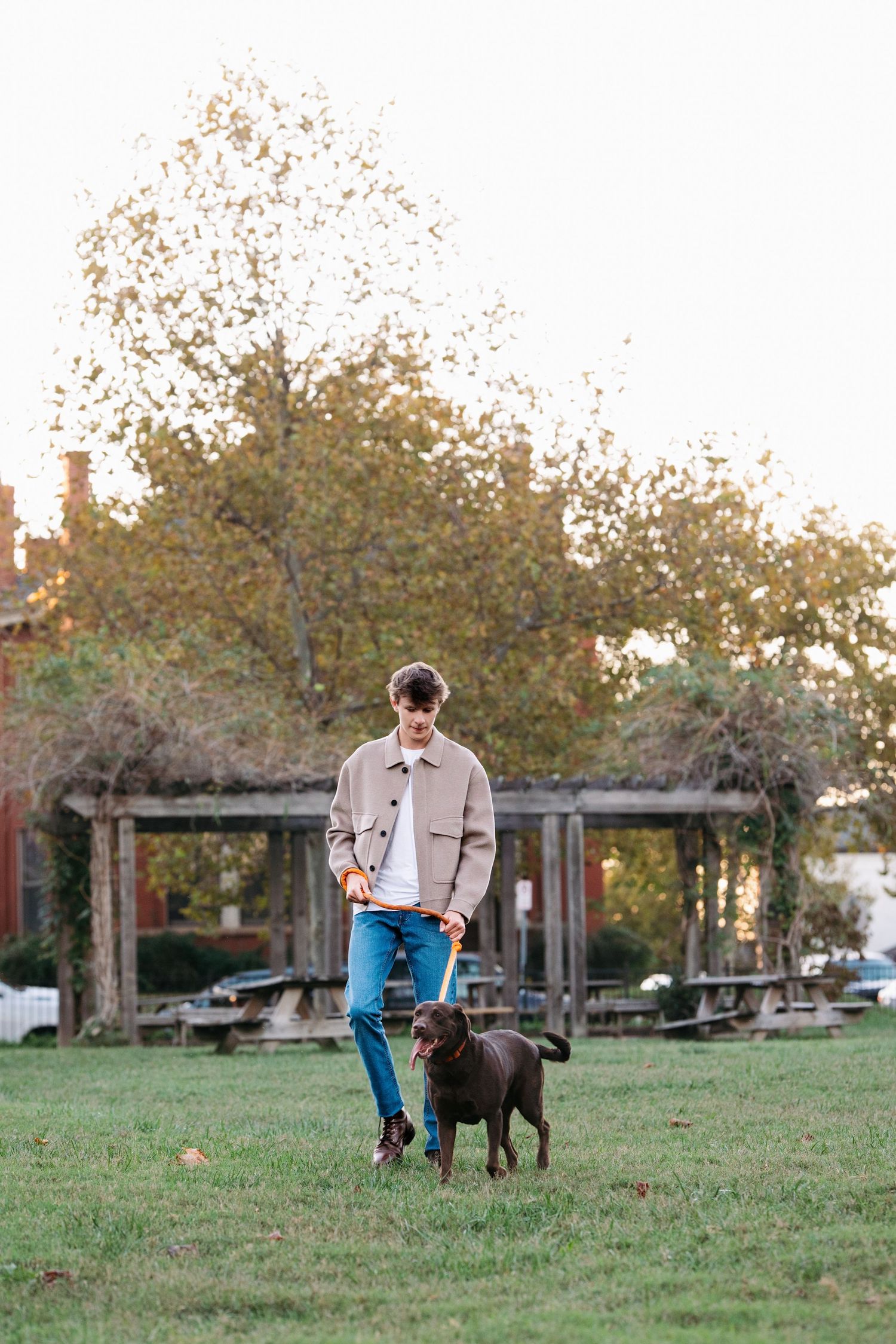 Dog walking with senior guy through autumn park with fallen leaves. Middle TN senior photographer.