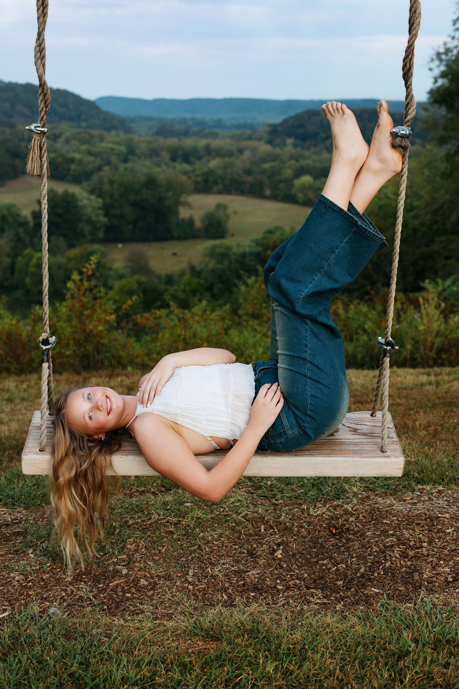 A playful sequence of someone swinging and flipping upside down on a wooden swing with rolling hills in the background.
