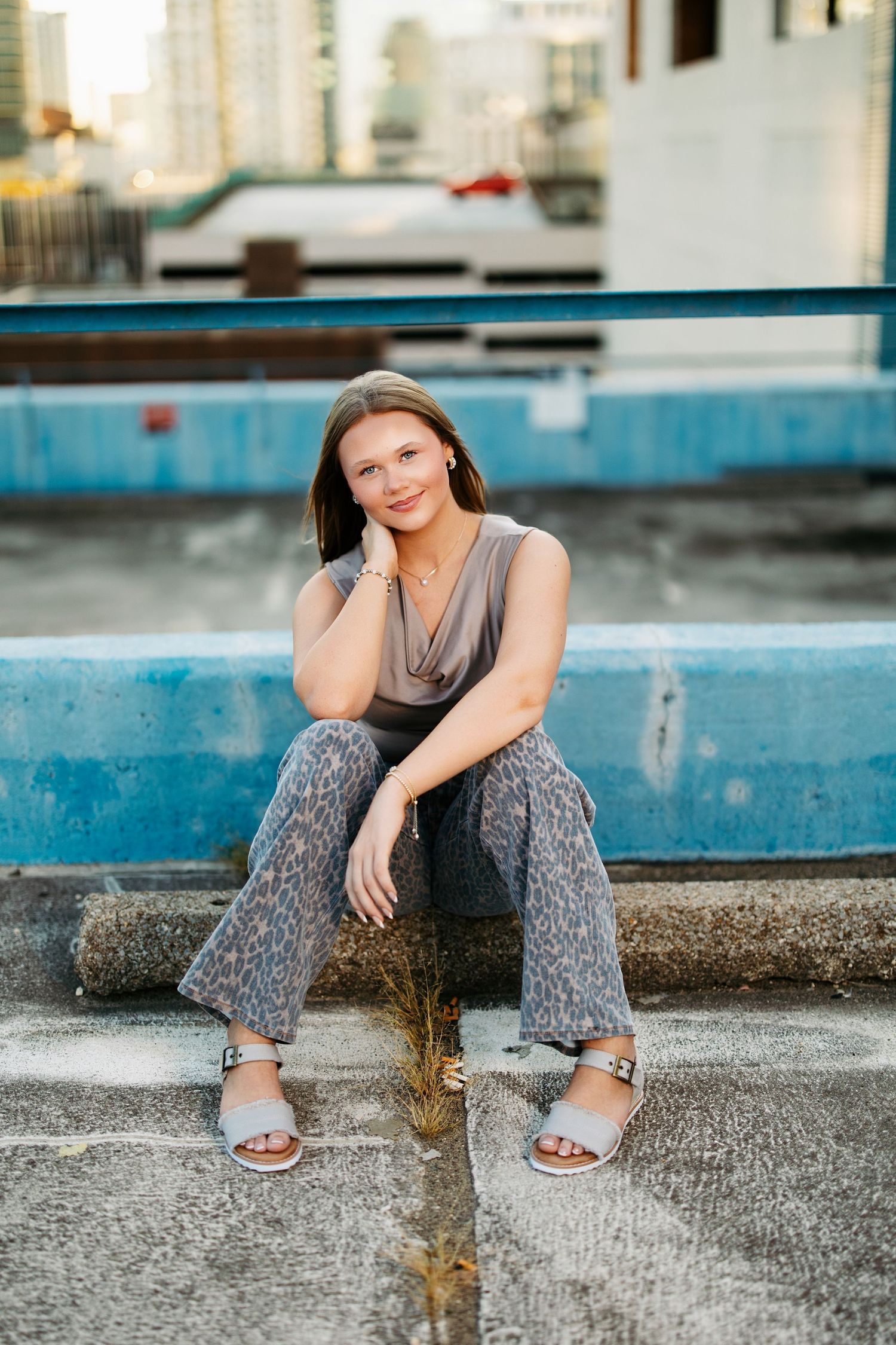 Person in patterned pants sits thoughtfully on concrete ledge near pool in casual outdoor setting.