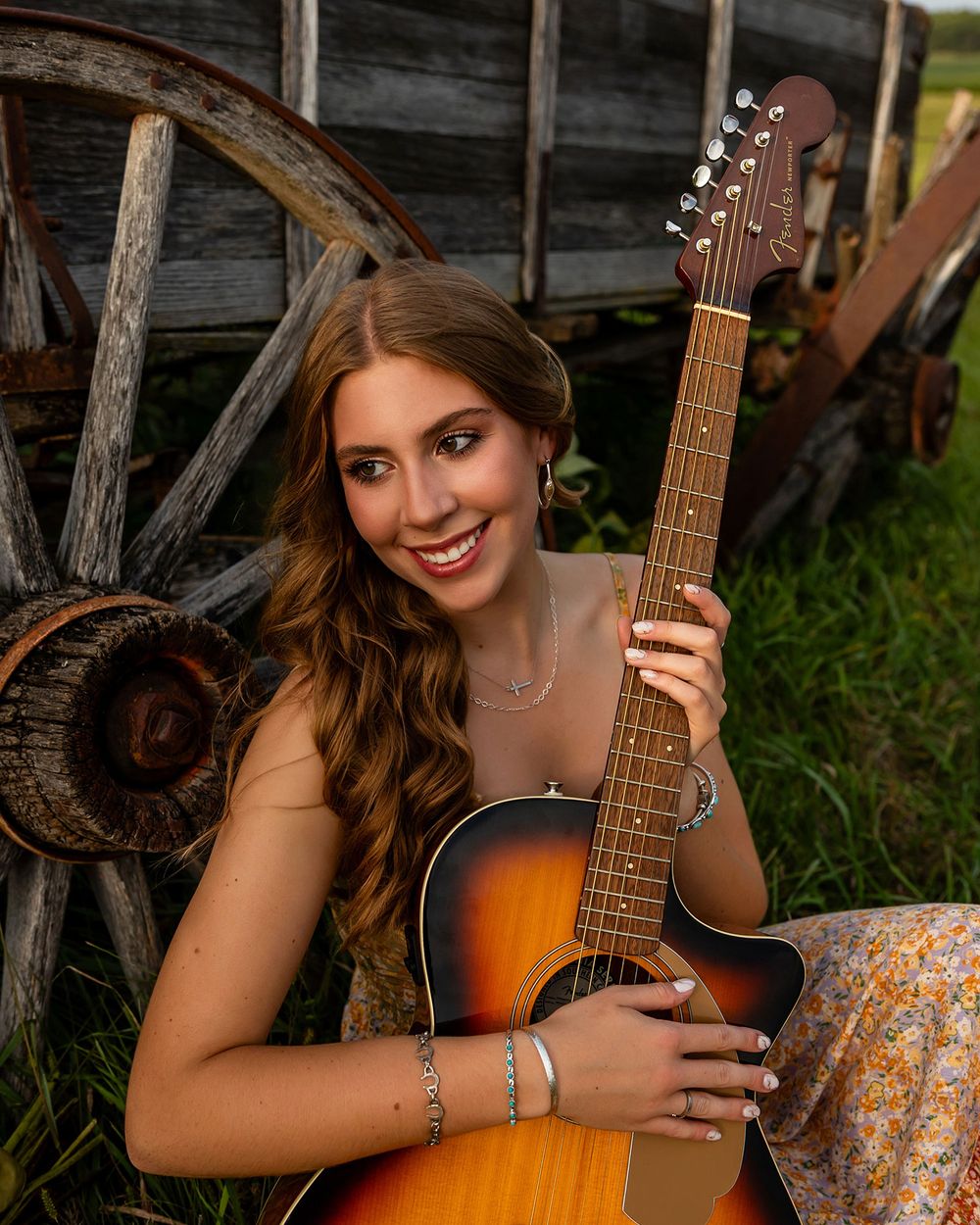 Acoustic guitar player poses outdoors by rustic wooden wagon wheel in a natural setting at sunset in Omaha, NE. - by BrightSide Photography