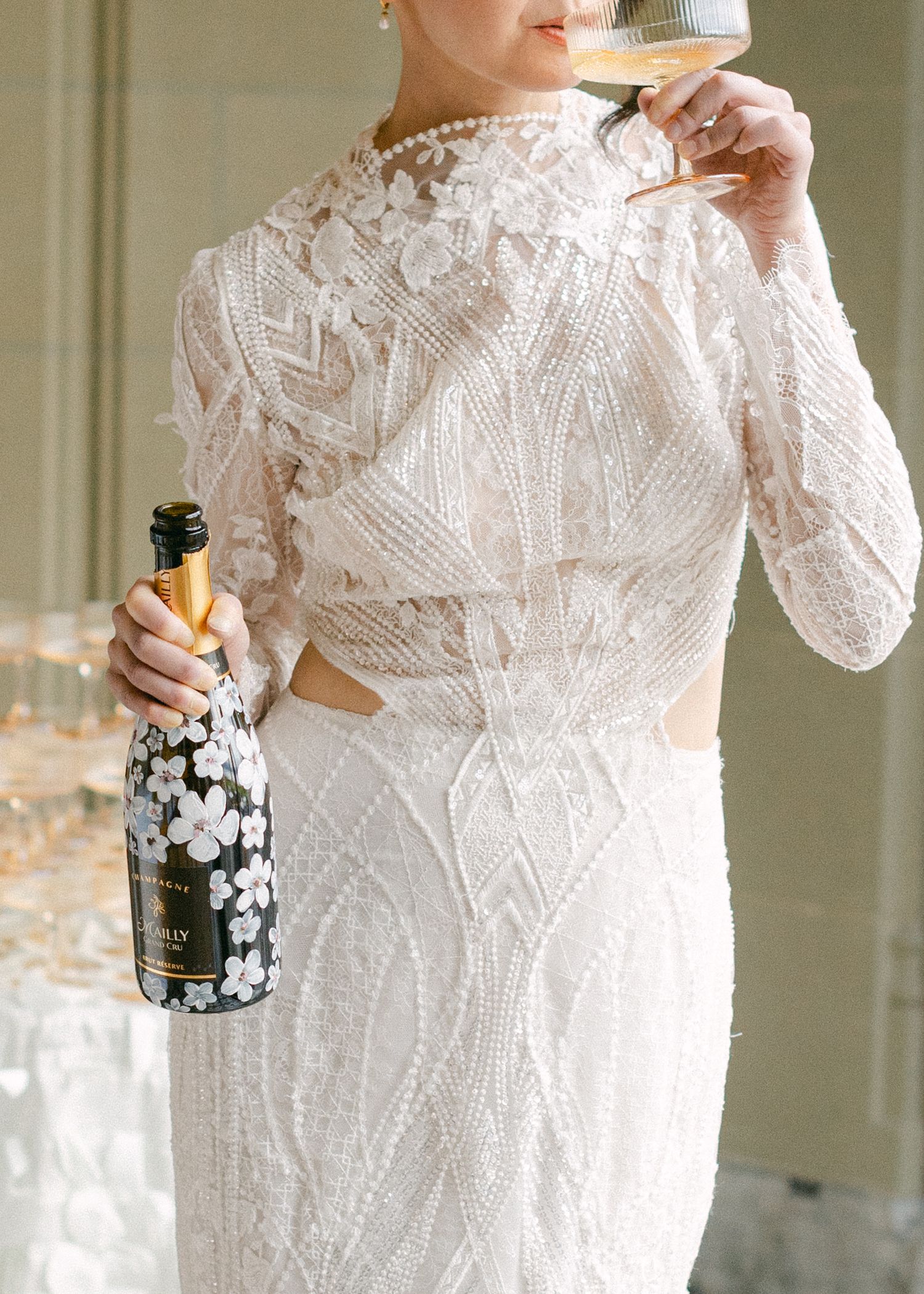 A bride holding a bottle of Champagne in a custom designed champagne bottle. She is wearing a white dress with beading.