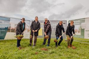 A group of people planting trees together in a grassy field next to a modern building.