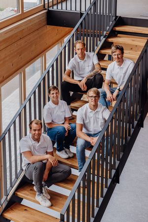 Group of people sitting on wooden stairs with black metal railings in a modern interior setting.