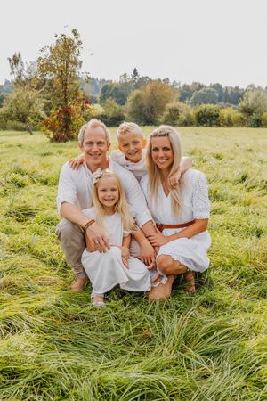 Vierköpfige Familie posiert zusammen auf einem hohen Grasfeld an einem sonnigen Tag.