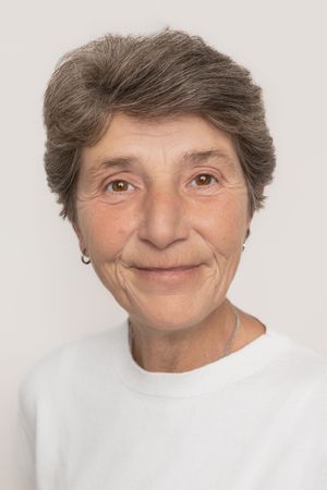 Portrait of a mature woman with short gray hair wearing a white top against a light backdrop.