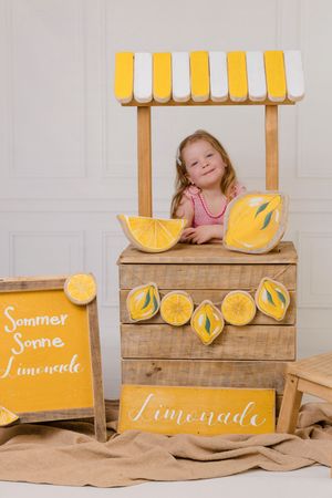 A rustic wooden lemonade stand decorated with yellow citrus slices and burlap fabric creates a charming summer scene.