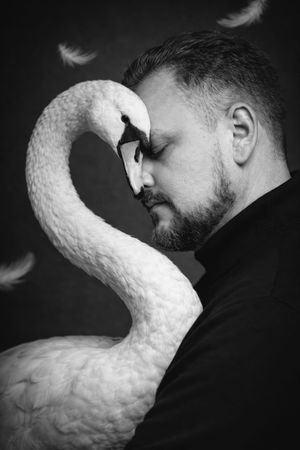 Artistic black and white portrait showing a person in profile next to an elegant white swan, with floating feathers.