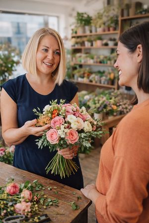 Two people share a joyful moment in a flower shop as they examine a beautiful bouquet of pink and white roses.