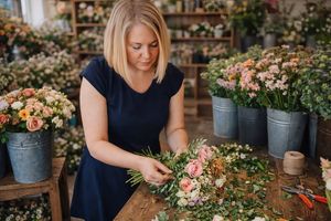 Florist arranging colorful fresh flowers in metal buckets at a rustic wooden workspace.
