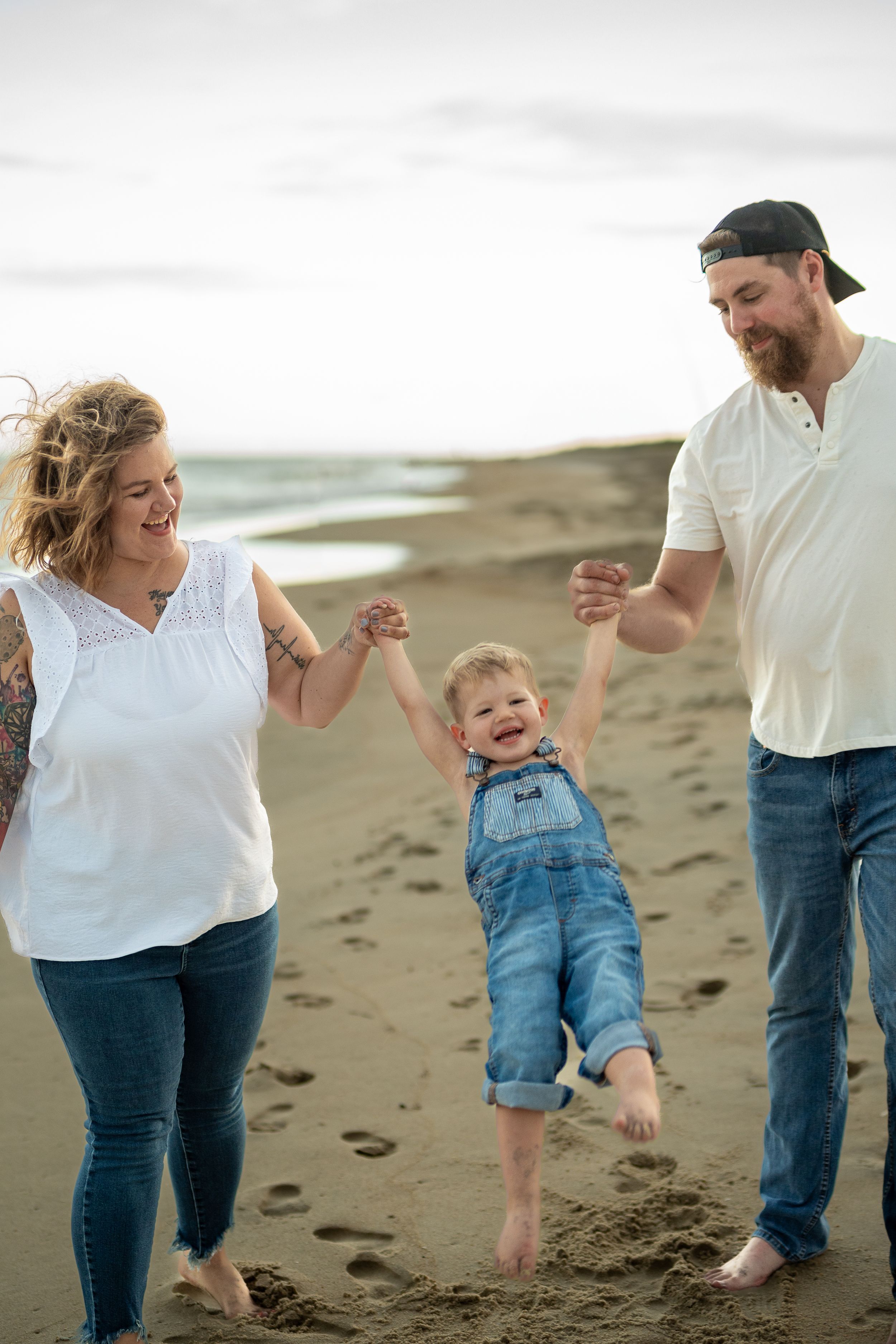 A joyful moment on the beach as a family swings their child between them while walking.