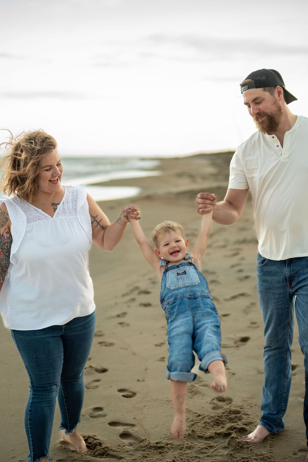 A joyful moment on the beach as a family swings their child between them while walking.