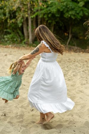 Two figures in white and mint green dresses dance gracefully together on a sandy beach at sunset.