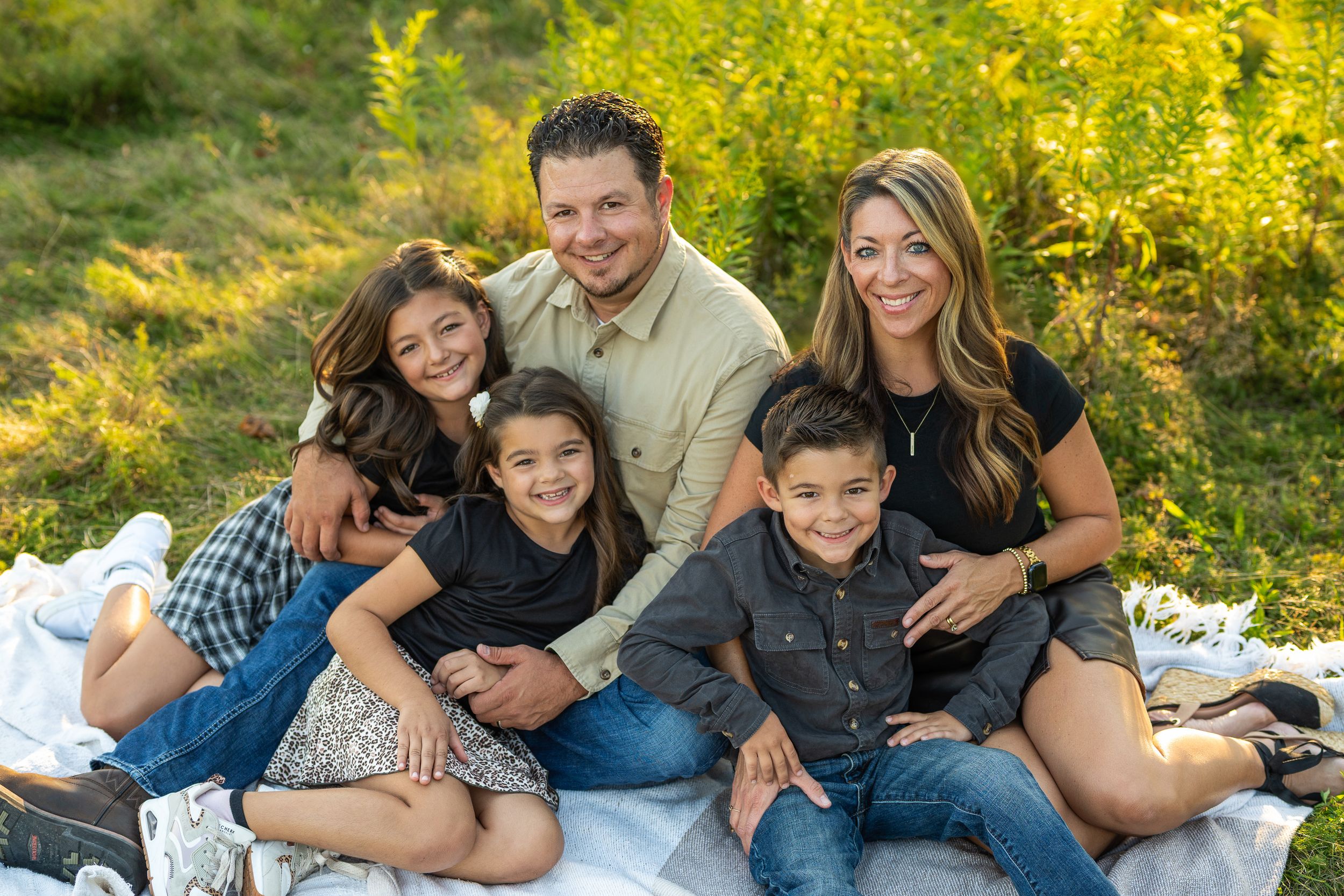 A family with their dogs poses together on grass during a golden hour outdoor photo session.