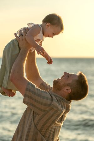 Parent and child playing together at sunset by the ocean in a heartwarming moment of connection and joy.