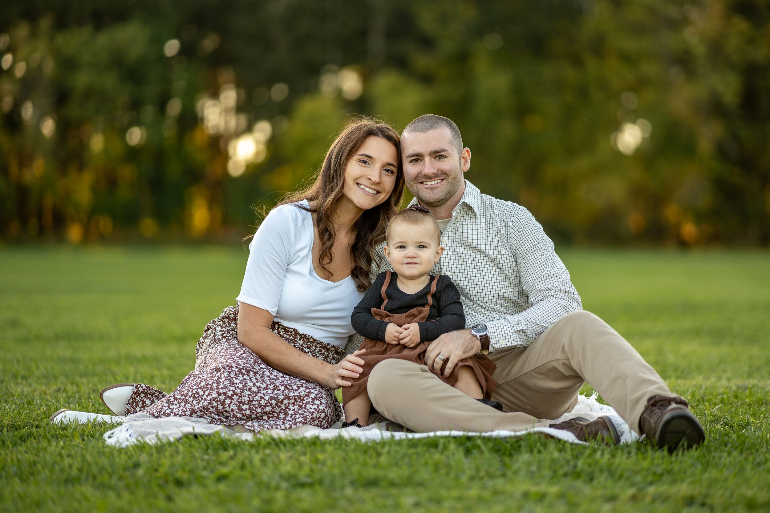 Family sitting together on a blanket for an outdoor portrait session in a park during golden hour.
