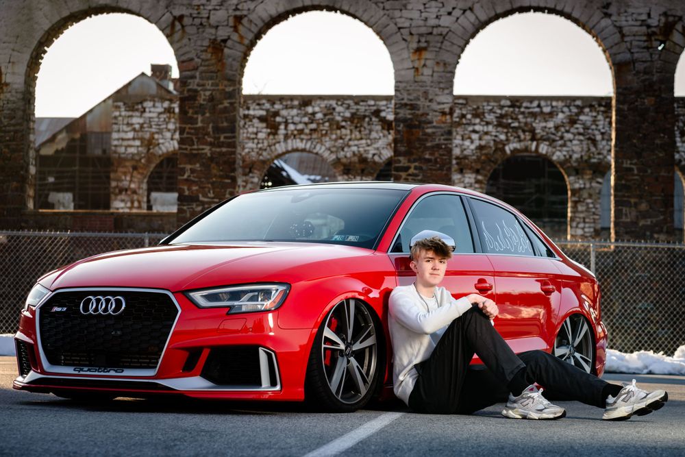 A red Audi RS3 parked in front of historic stone arches.