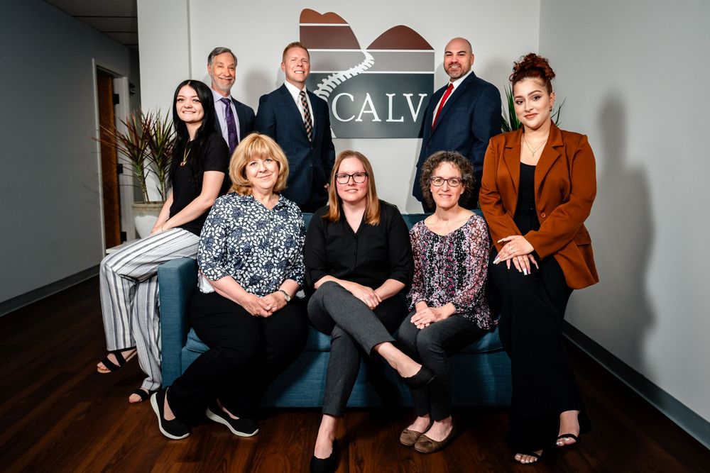 Professional business team members pose together in an office setting with CALV signage.