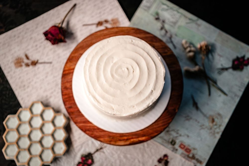 A white frosted cake on wooden stand with honeycomb decorations and dried roses.