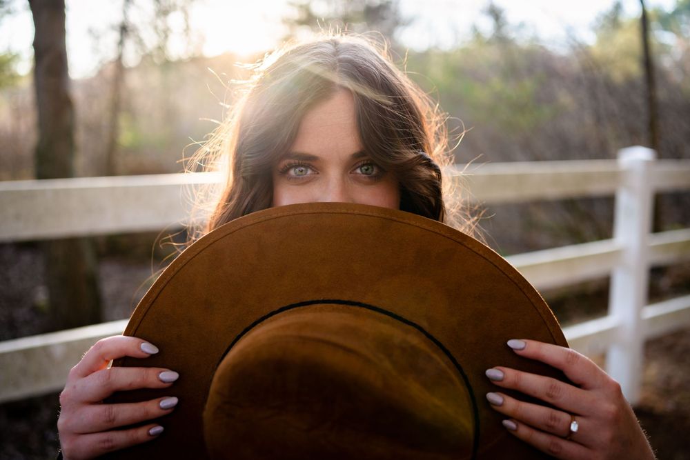 A brown felt hat held up in front of a wooden fence at sunset.