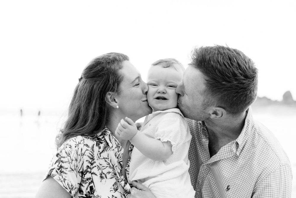 Family sharing intimate moment with child on misty beach in black and white.