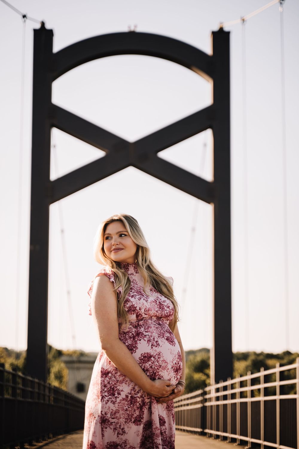 Pregnant woman smiling on a bridge at golden hour, cradling her baby bump. Nashville Tennessee Pregnancy maternity family photographer photo