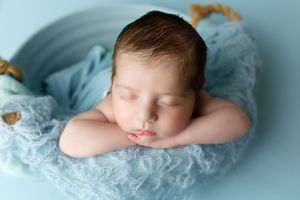 A sleeping newborn rests peacefully on a soft light blue blanket in a professional studio portrait.