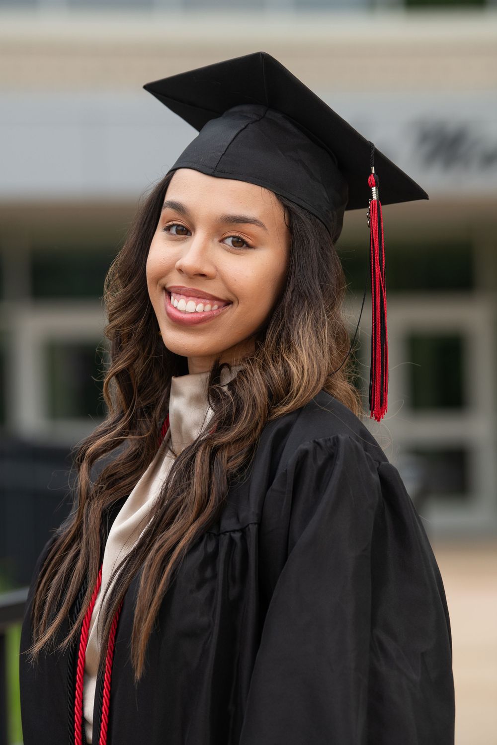 College graduate wearing black cap and gown with red tassel smiles during graduation ceremony.