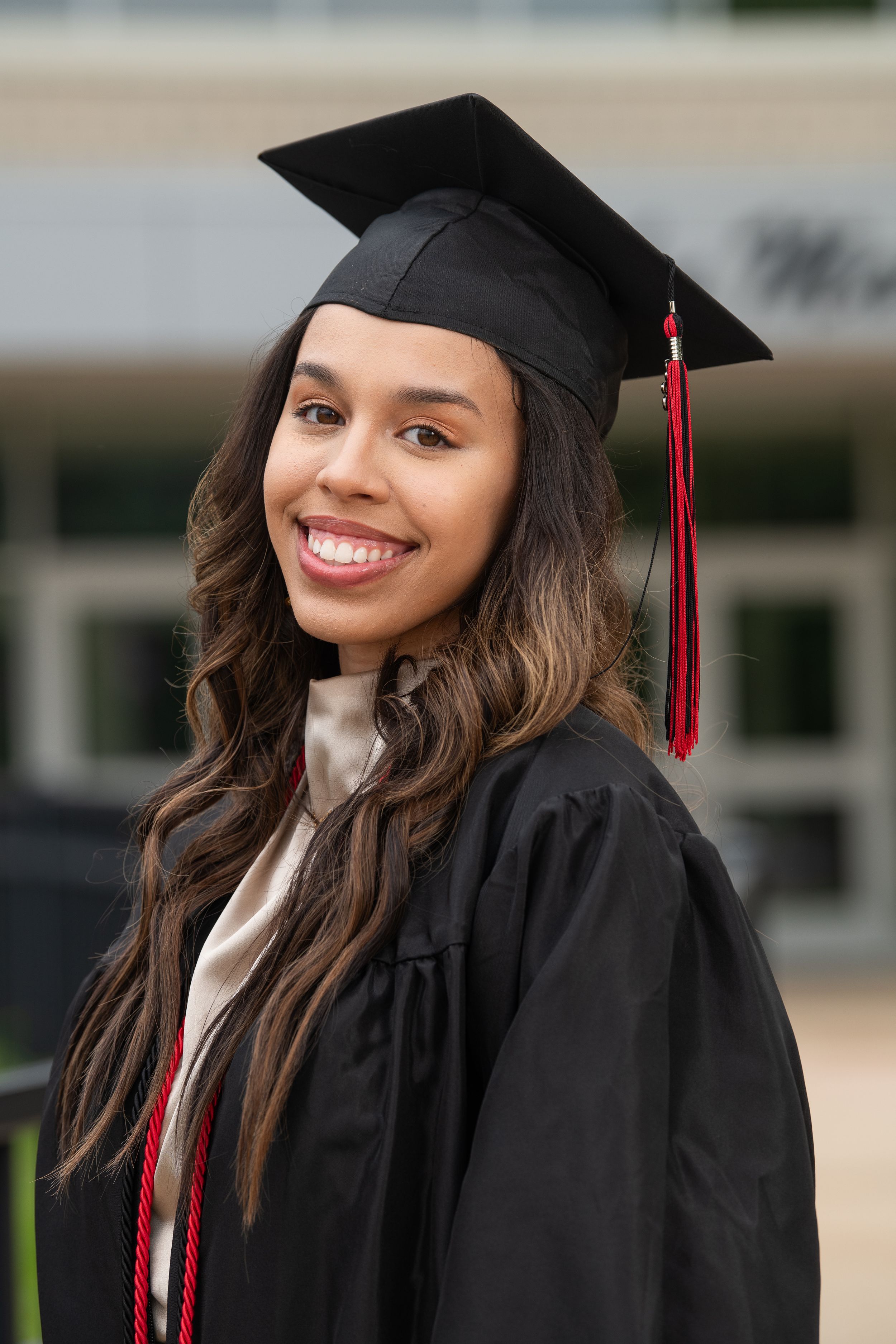 College graduate wearing black cap and gown with red tassel smiles during graduation ceremony.